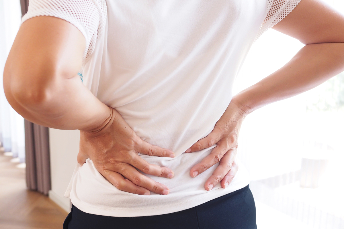Person holding their lower back with both hands, wearing a white shirt.